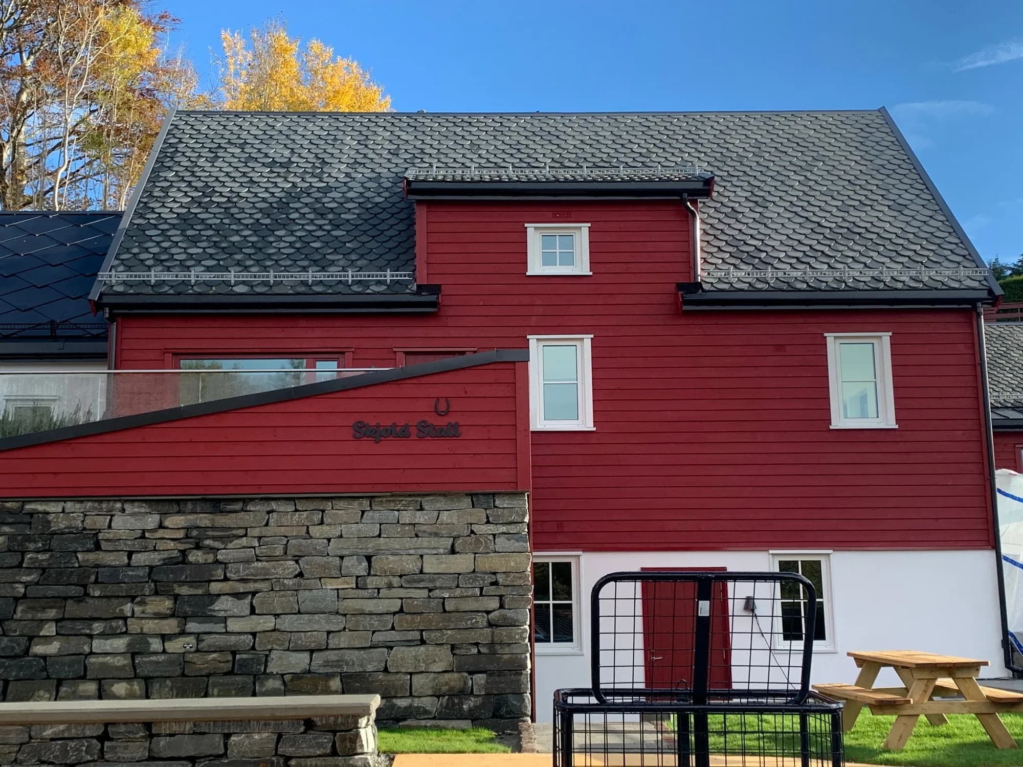 Rødmalt trehus med hvite vinduer over en steinmur